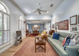 A well-lit living room with a green sofa, coffee table, wall art, and an adjoining dining area with a chandelier and wooden dining table.