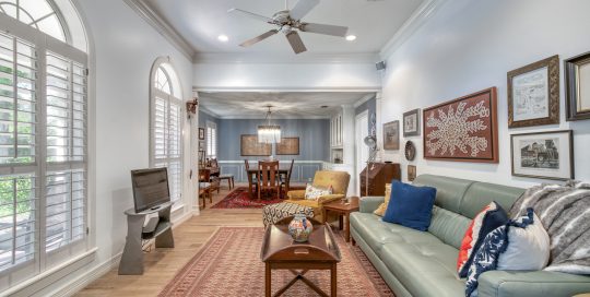 A well-lit living room with a green sofa, coffee table, wall art, and an adjoining dining area with a chandelier and wooden dining table.