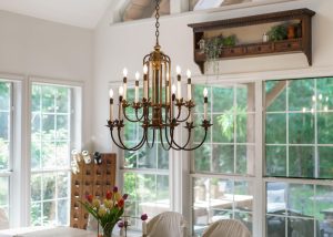 A brass chandelier hangs over a dining table with a vase of tulips; large windows in the background let in natural light.