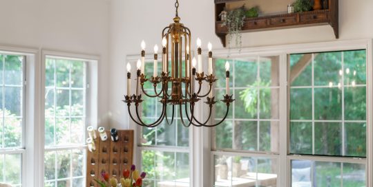 A brass chandelier hangs over a dining table with a vase of tulips; large windows in the background let in natural light.