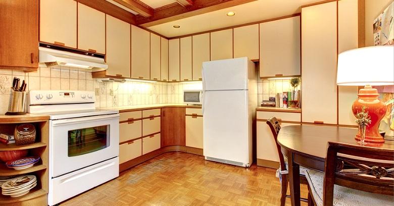 Kitchen with beige cabinets, white appliances including a stove and refrigerator, small dining table with chairs, and tiled backsplash.