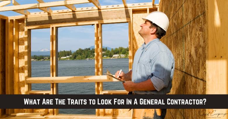 A man in a hard hat holds a clipboard while inspecting the wooden frame of a building under construction by a lake.
