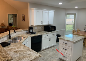 Modern kitchen with white cabinets, granite countertops, stainless steel sink, black appliances, and a small island; a red arrow points to a drawer on the island.