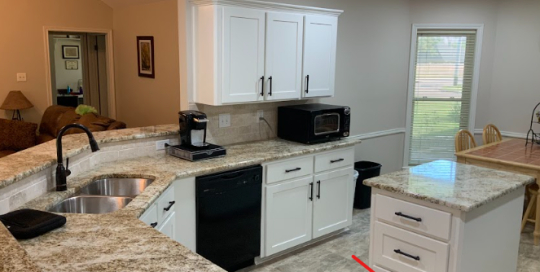 Modern kitchen with white cabinets, granite countertops, stainless steel sink, black appliances, and a small island; a red arrow points to a drawer on the island.